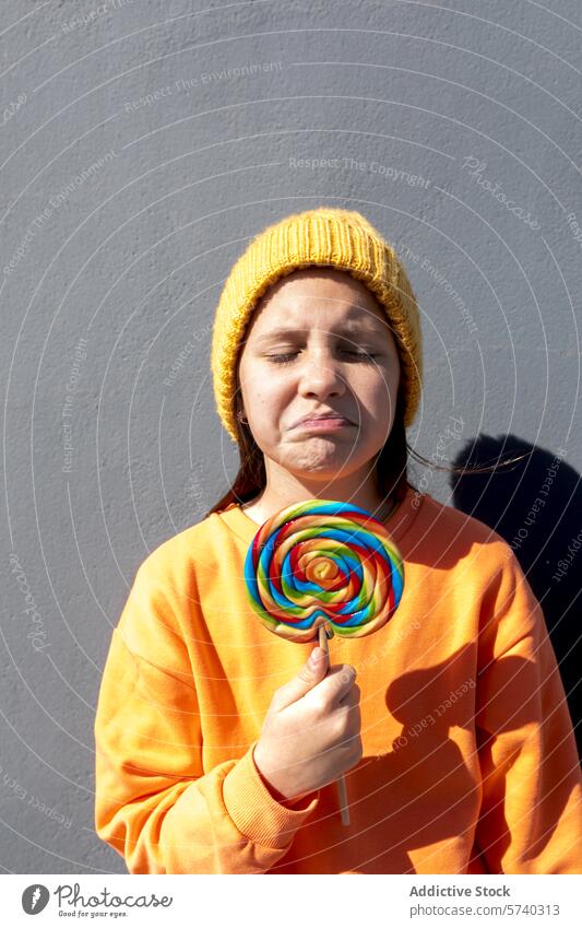 Young person with colorful lollipop on a sunny day young beanie sweatshirt orange yellow frown casual outdoor unhappy sweet treat candy sugar snack multicolored