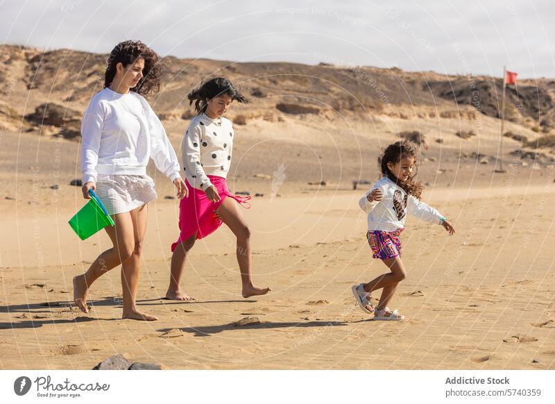 A loving single mother strolls along the beach with her two young daughters, the youngest gleefully running ahead family children play sand woman summer