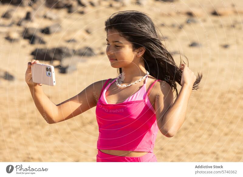 A girl in vibrant pink beachwear confidently takes a selfie on the sandy shores, capturing the essence of a sunny beach day phone summer child capture leisure