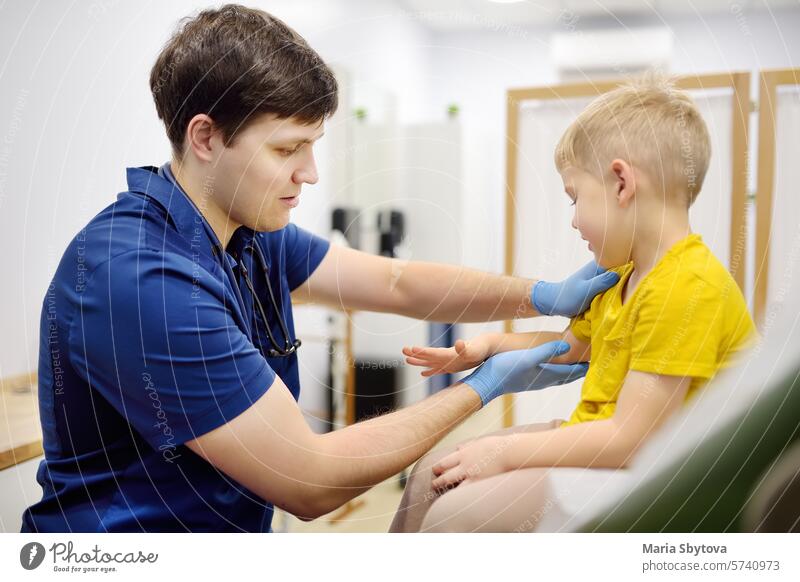 A cute toddler boy with his mother are at an appointment with a pediatrician. The doctor orthopedist is examines joints of a little patient.
