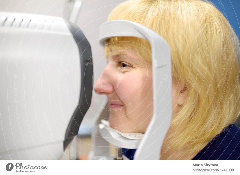 Portrait of mature woman during visit to optometrist for microscopic analysis of eyelids, sclera, conjunctiva, iris, lens, cornea. Exam of patient fundus by ophthalmologist using retinal scanner