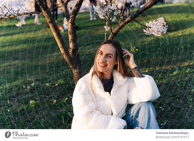 Woman enjoying spring sitting on grass in city park among flowering trees young garden woman nature cherry outdoor blossom blooming beauty beautiful long scenic