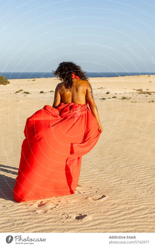 Anonymous elegant woman in red dress strolling on desert dunes walking looking away elegance fashion sand sea serene nature tranquility outdoor landscape