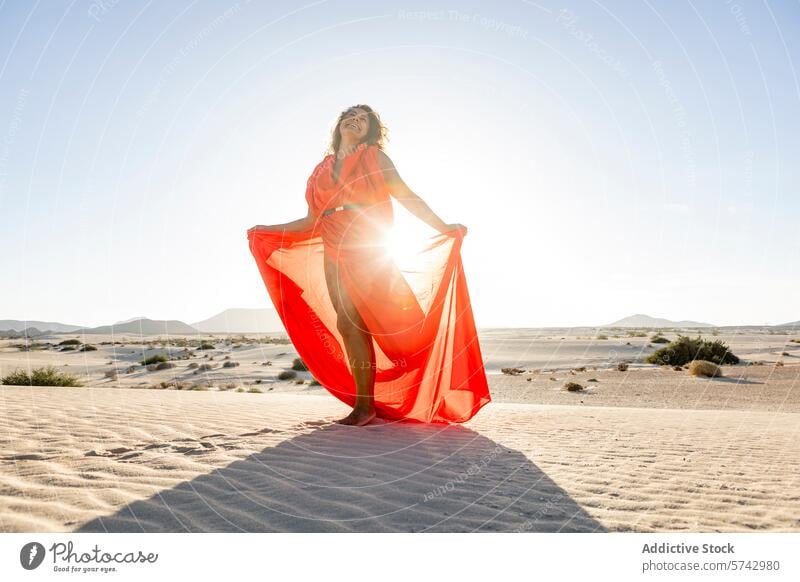 Woman in vibrant red dress stands on sandy dunes woman desert elegant pose sunlight golden flowing fabric fashion outdoor serene tranquil beauty elegance style