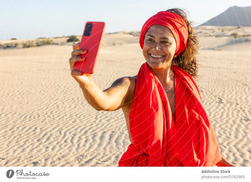 Joyful woman in red capturing selfie in the desert dress dunes mobile phone smile happiness vibrant headscarf gadget device sand looking at camera joy sunshine