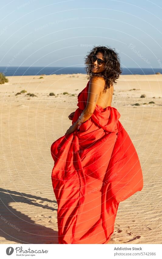 Joyful woman in red looking away on desert dunes red dress sandy sea looking at camera cheerful joyful flowing dress fashion nature outdoor sunny summer beach