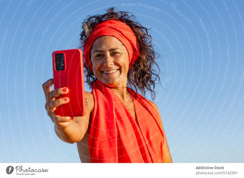 Woman in Red Taking a Selfie in the Desert woman red dress desert dune selfie mobile phone blue sky clear bright cheerful gadget device technology photography
