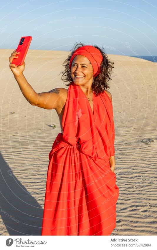 Woman in red dress taking selfie in the desert woman dunes smartphone sand headscarf smiling joy vibrant colorful outdoor nature scenic sunlight day summer