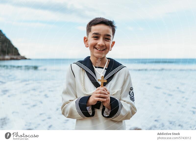 A beaming boy holding a crucifix stands by the sea, dressed in his First Communion sailor suit, embodying joy and faith smile ocean celebration child waterfront