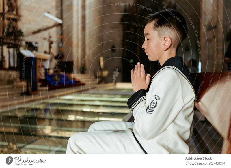 A solemn young boy sits in a church pew, hands clasped in prayer, during his First Communion ceremony, a sacred rite of passage white suit navy faith Christian