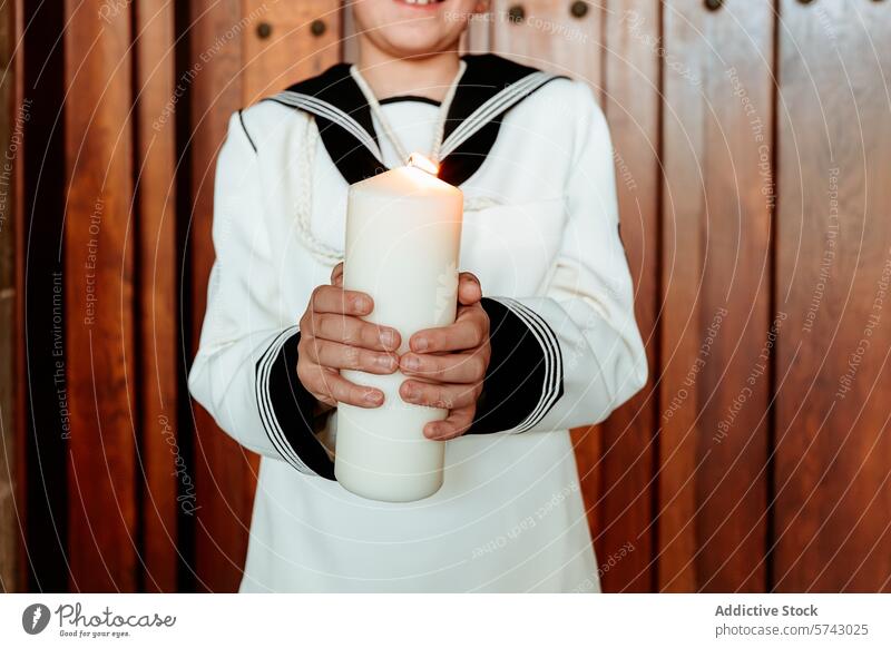 A close-up of anonymous child's hands tenderly holding a lit candle, a symbol of faith during the First Communion celebration communion embrace white suit