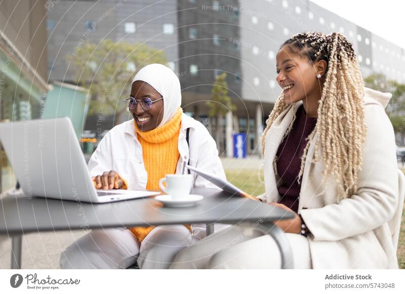 Smiling black women with laptop at outdoor cafe woman female african muslim hijab friendship device gadget smiling conversation connectivity city urban