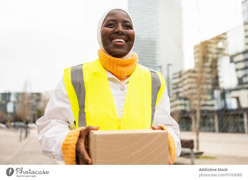 Smiling African American woman with parcel in urban setting female african american city buildings background smiling cheerful delivery worker high-visibility