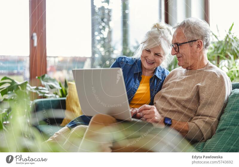 Senior couple using laptop while sitting on sofa in living room at home people caucasian grey hair casual day portrait indoors real people white people adult