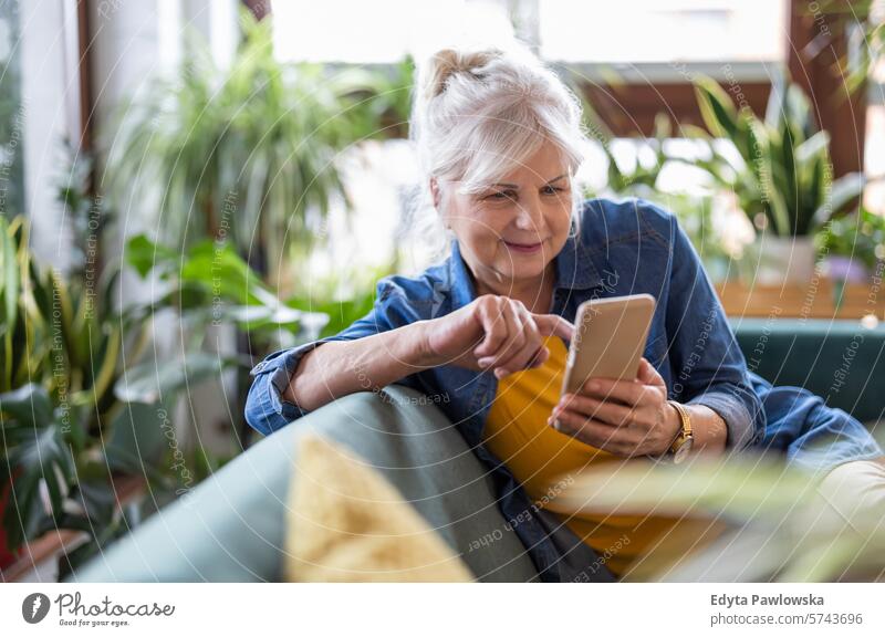 Smiling senior woman using smart phone while sitting on sofa at home people casual day portrait indoors real people white people adult mature retired old