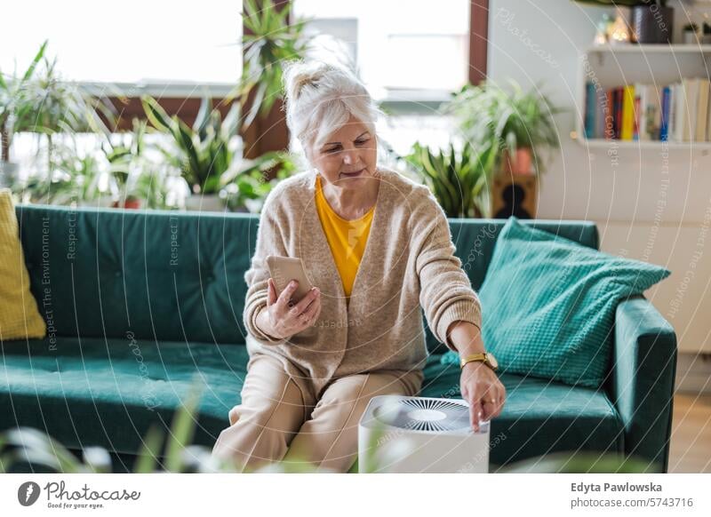 An elderly woman uses her smartphone to set up an air purifier at home Air purifier Air pollution Technology Modern by phone Sofa Living room Living or residing