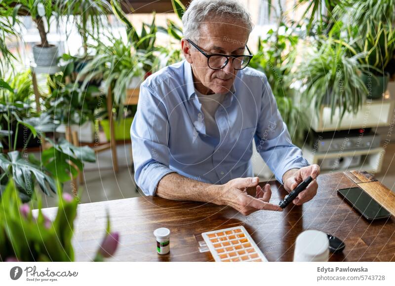 Mature man checking his blood sugar level while sitting at home glaucometer hands table health patient illness blood sugar test examining healthcare medicine
