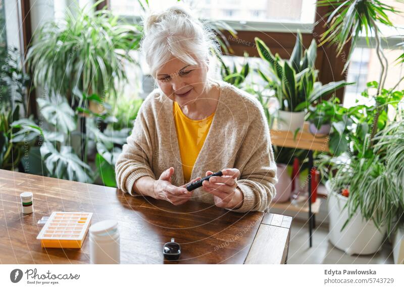 Elderly woman checking her blood sugar level while sitting at home glaucometer hands table health patient illness blood sugar test examining healthcare medicine