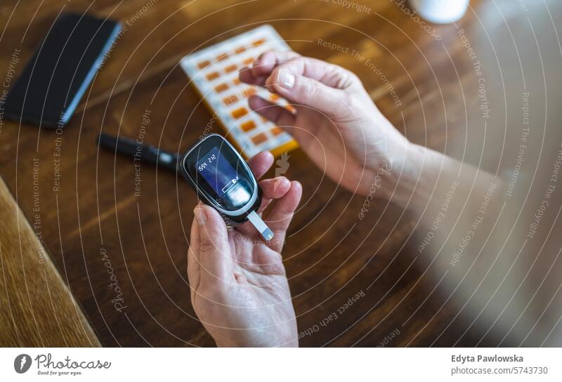 Elderly woman checking her blood sugar level while sitting at home glaucometer hands table health patient illness blood sugar test examining healthcare medicine