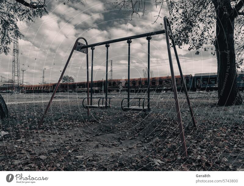empty swings on an empty playground without people against the background of burnt trains in Ukraine Donetsk Kherson Kyiv Lugansk Mariupol Russia Zaporozhye