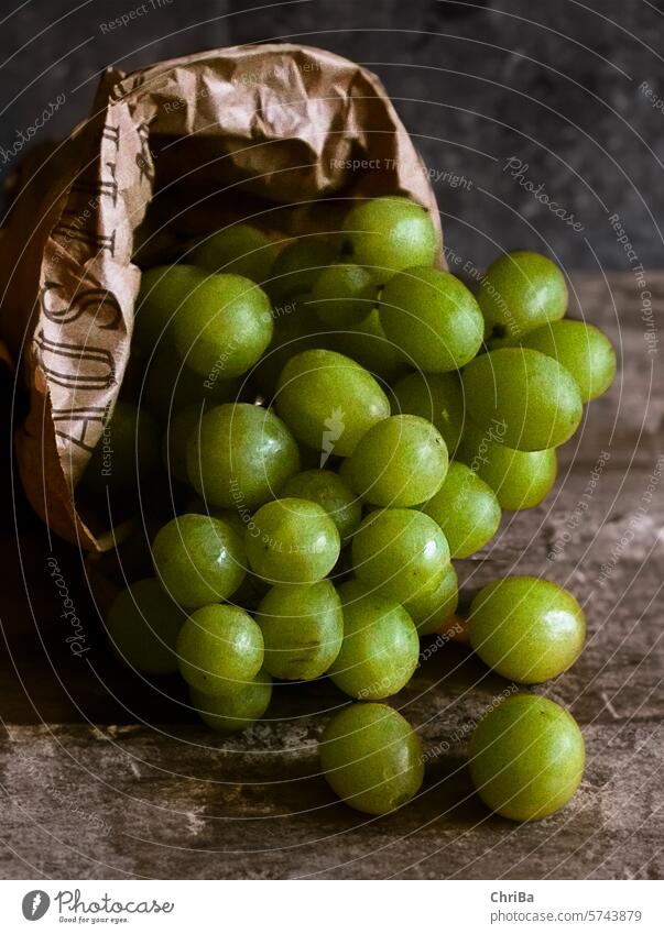 Green grapes fall out of a brown fruit bag onto a rustic table Bunch of grapes Sour naturally Brown paper bag Paper Markets Table Rustic Delicious salubriously