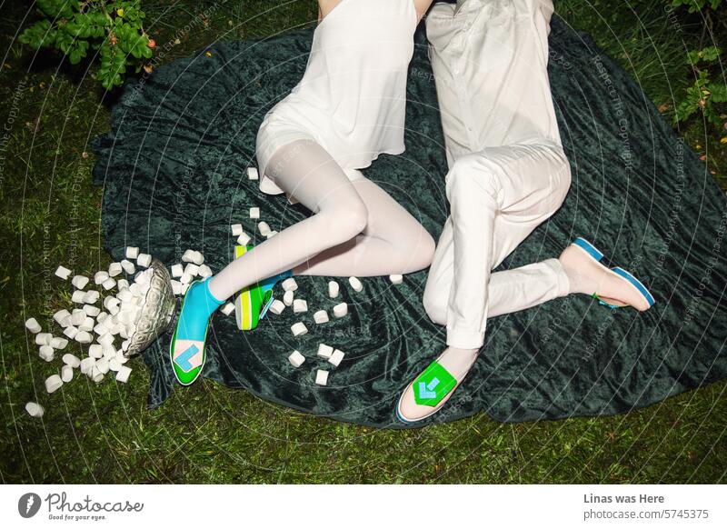Two beautiful people, dressed in white with some avant-garde fancy shoes, are on a date. They enjoy a picnic outdoors at night, with marshmallows and love in the air. Is it just a date, or has romance already blossomed?