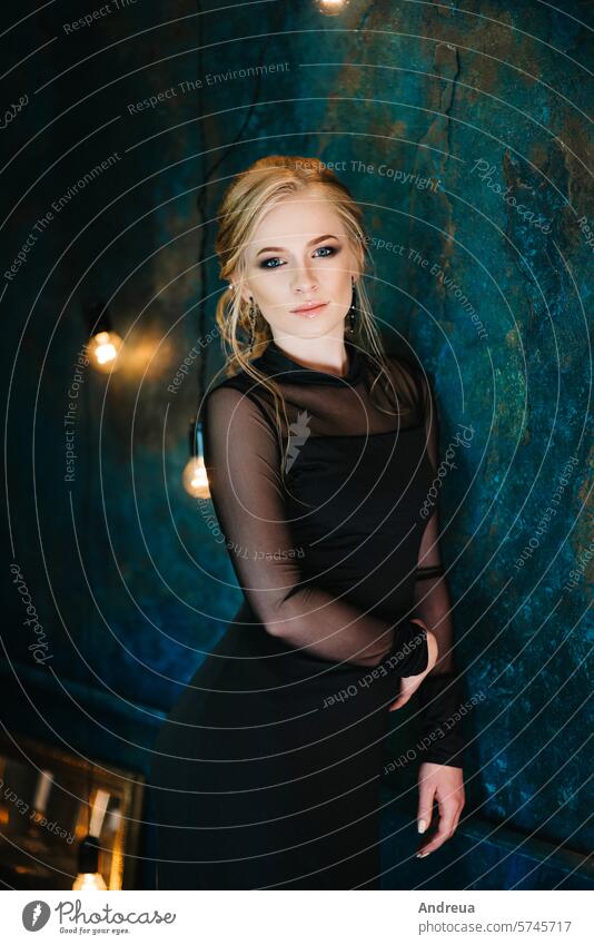 Blonde girl with blue eyes in a black dress Girl blonde turquoise interior portrait sit stand close-up view fashion evening lights warm glazy gentle young one