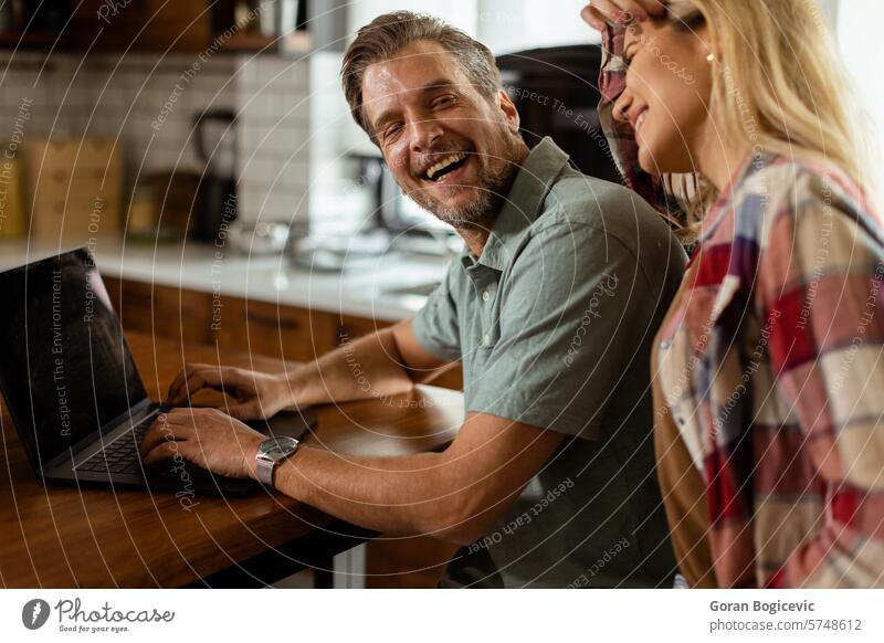 Cheerful couple enjoys a light-hearted moment in their sunny kitchen, working on laptop surrounded by a healthy breakfast laughing cheerful relationship morning