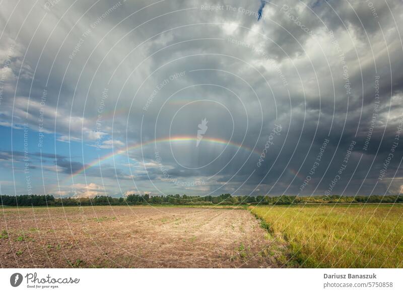 A rainbow in the cloudy sky over the rural fields meadow outdoor landscape overcast nature weather environment grass summer horizon blue green view light