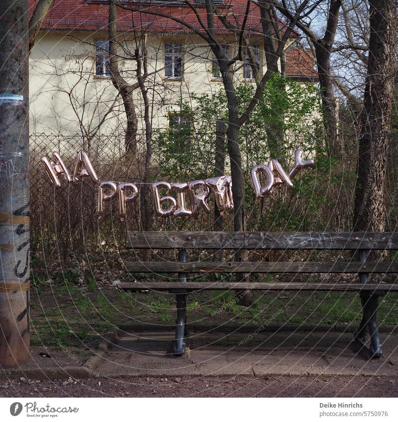 Golden Happy Birthday garland hangs slightly damaged over a park bench Birthday celebration Party Paper chain Decoration Park Park bench Berlin City Tradition