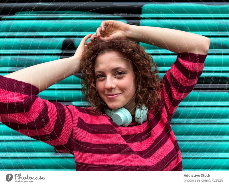 Young redhead woman with headphones enjoying the city vibe young smile happy vibrant teal background striped sweater casual urban lifestyle cheerful enjoyment