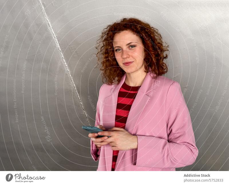 Business redhead woman with mobile phone against gray background smartphone businesswoman curly hair confident standing holding looking at camera smile