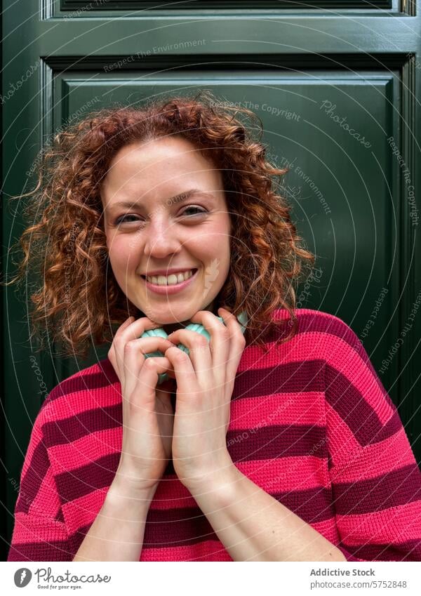 Smiling redhead woman in striped sweater against green door smile curly hair red hair happiness cheerfulness fashion portrait young adult bright colors