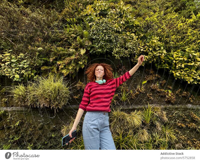 Young redhead woman enjoying nature surrounded by lush greenery happiness freedom vibrant plants wall curly hair stretching arms young adult leisure casual