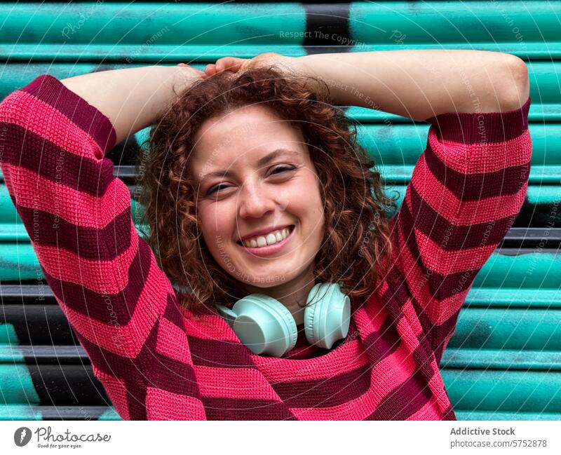 Joyful redhead woman with headphones enjoys a relaxed moment smile joyful vibrant turquoise background sweater striped cheerful young fashion casual leisure