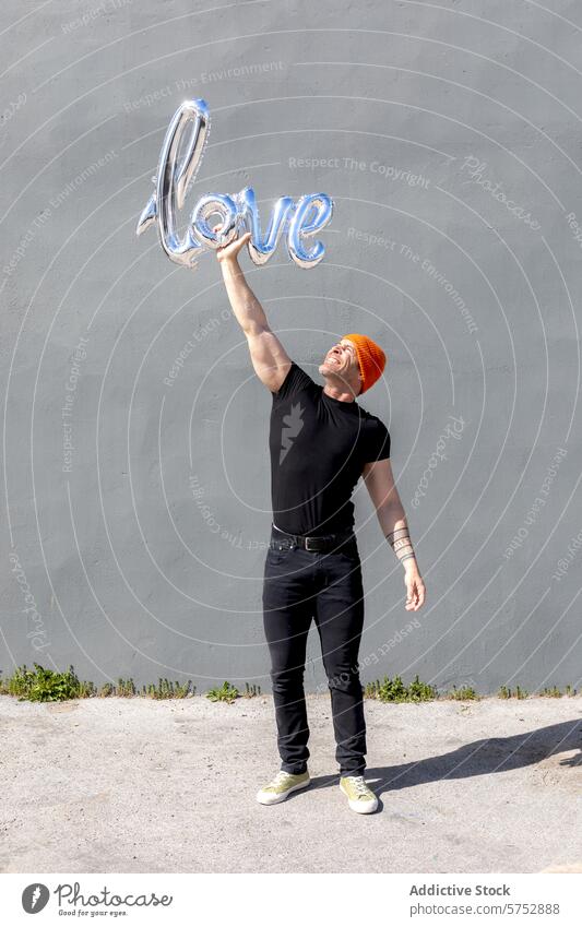 Man holding a love balloon with joyful expression man happy shiny black outfit orange beanie wall celebration romantic concept affection emotion valentine