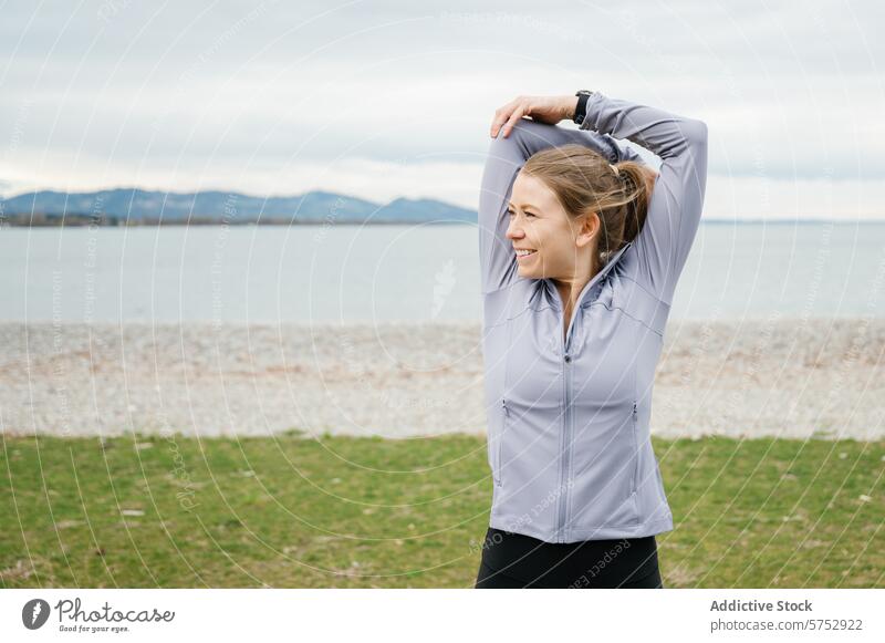 Woman stretching by the sea during outdoor workout woman fitness athletic wear smile tricep pebble beach cloudy sky exercise health active lifestyle training