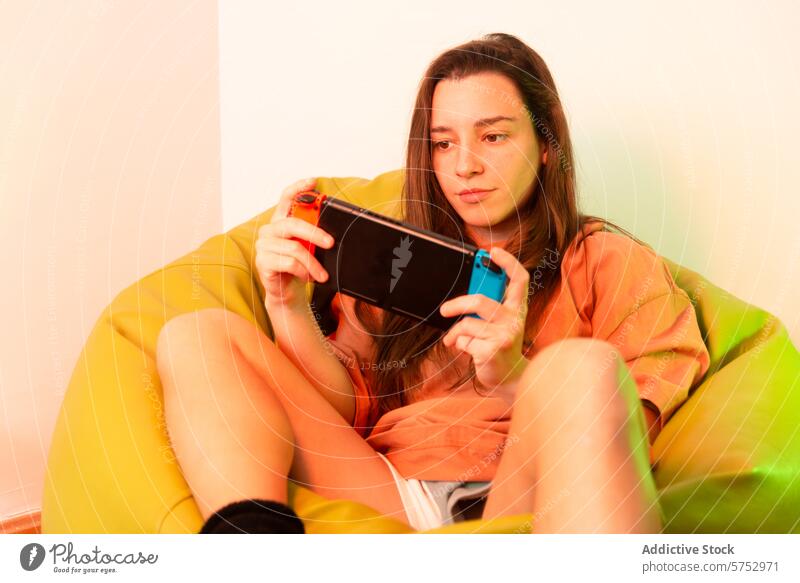 A focused individual lounges in a multicolored bean bag while engaging with a game on a handheld gaming device, embodying casual home entertainment session