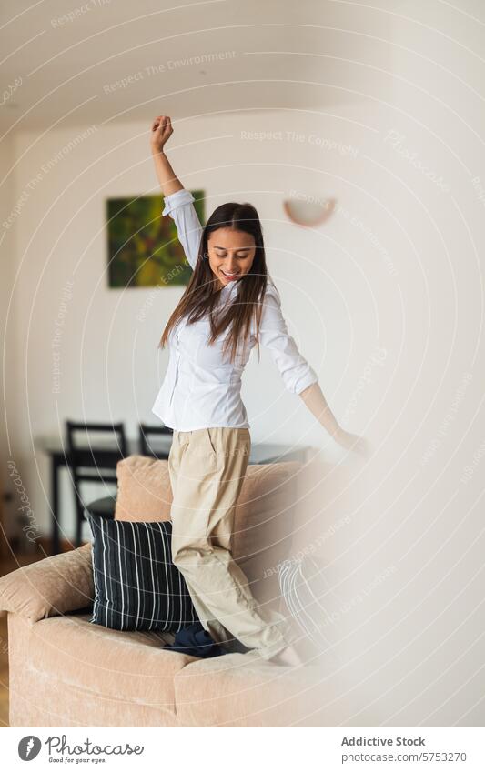 Joyful young woman dancing alone at home joy cheerful happiness freedom living room bright enjoyment adult leisure activity white shirt beige pants indoor