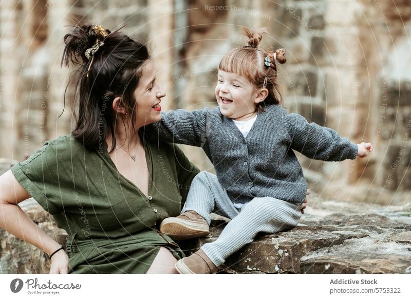 Joyful Moment Between Mother and Child Outdoors mother child laughing joy bonding casual outdoors stone ledge heartwarming sharing moment rustic woman girl