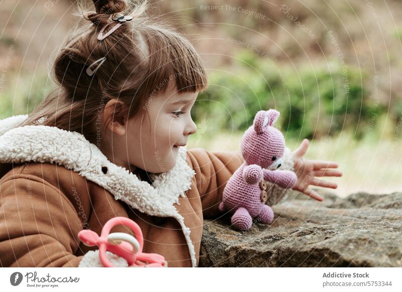 Young girl playing with a knitted bunny outdoors child imagination joy handmade stuffed rabbit toy cozy jacket stone surface playtime nature childhood fun