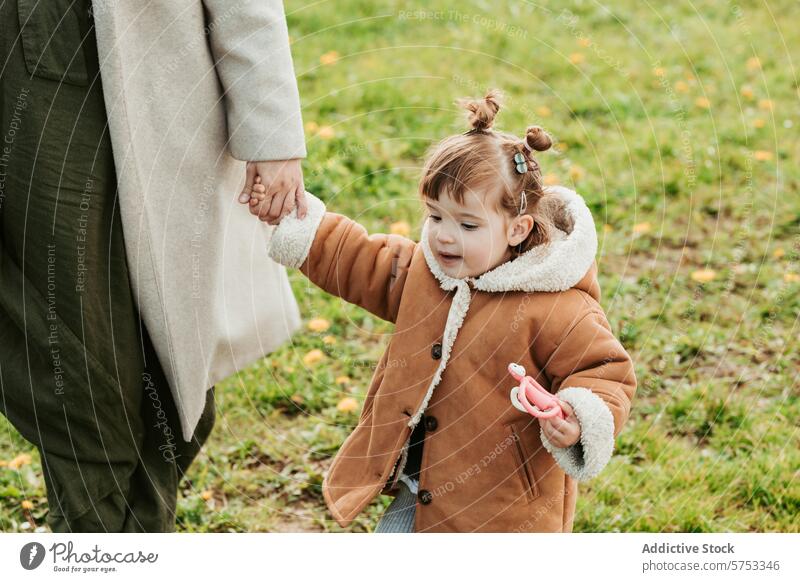 Toddler holding hands with parent on a grassy field toddler walking yellow flower joy expression adult joyful outdoor nature bonding child care guidance support
