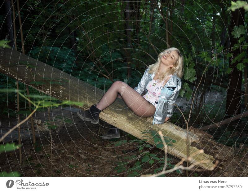 In a wild, green forest, a gorgeous blonde girl finds the perfect setting to embrace her wild and free spirit. She revels in her own company, displaying her pretty long legs and beautiful face. A fallen tree provides a comfortable seat for her.