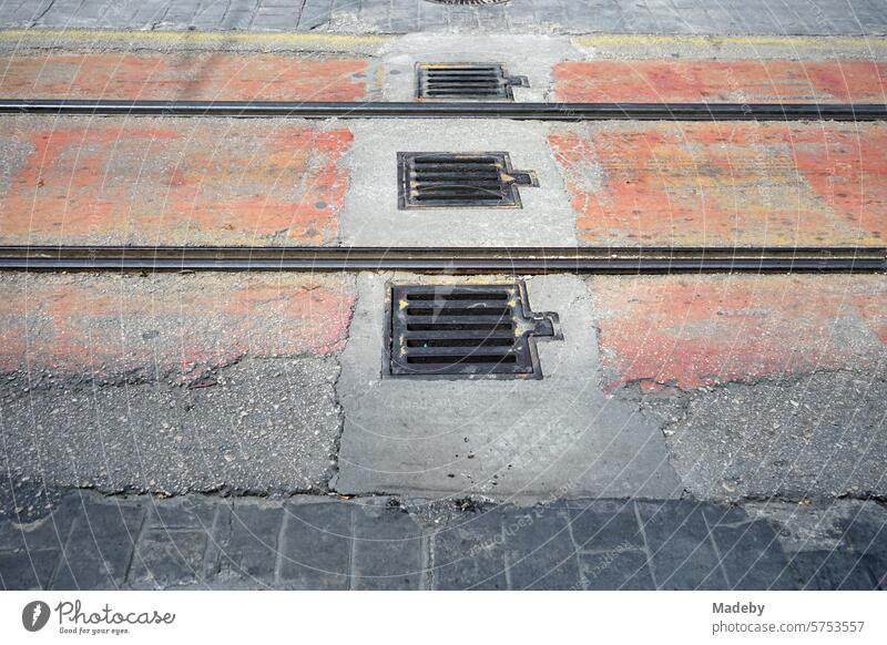 Rails and tracks of the streetcar with manhole cover or manhole cover between old gray and crumbling paving stone in a pedestrian zone in sunshine in Bursa at the Uludag Mountains in Turkey