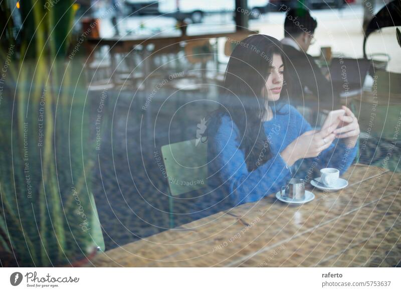 Woman texting at a cafe woman smartphone blue sweater coffee cup saucer sitting window reflection relaxed alone technology urban lifestyle female young adult
