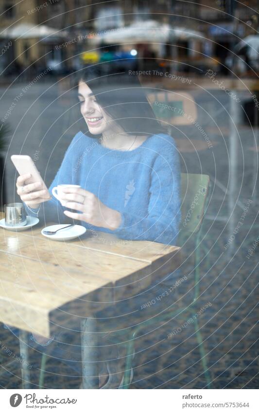 Woman texting at a cafe woman smartphone blue sweater coffee cup saucer sitting window reflection relaxed alone technology urban lifestyle female young adult