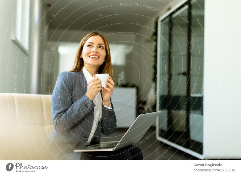 Elegant businesswoman enjoying a peaceful coffee break on sunny office morning laptop sunlight professional work elegant poised technology sipping engaging