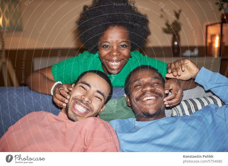 Front view portrait of diverse group of three friends with Black young woman smiling at camera during party shot with flash home Black woman Black man smile