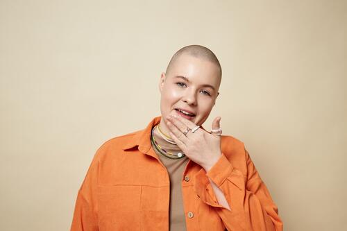 Portrait of confident bald young woman wearing bright orange jacket in studio female girl gen Z hair loss alopecia mouth lips lick cancer chemotherapy beauty