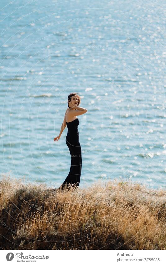 tall girl model in a black dress on the mountain hills high sea from above summer blue sky grass green yellow clay sunset horizon evening heat light walk